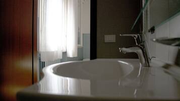 A bathroom with a white sink, a mirror, and a window with sheer curtains.