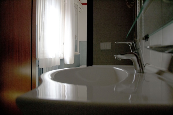A bathroom with a white sink, a mirror, and a window with sheer curtains.