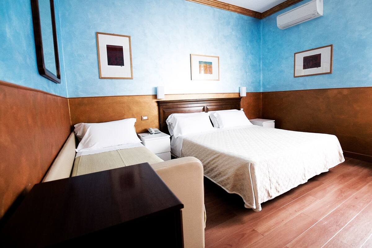 A hotel room with two beds, wooden paneling, and framed artwork on the walls.