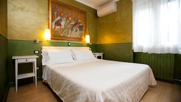 Habitación de hotel con una cama grande, dos mesitas de noche, un cuadro colgado en la pared y una ventana con cortinas traslúcidas.