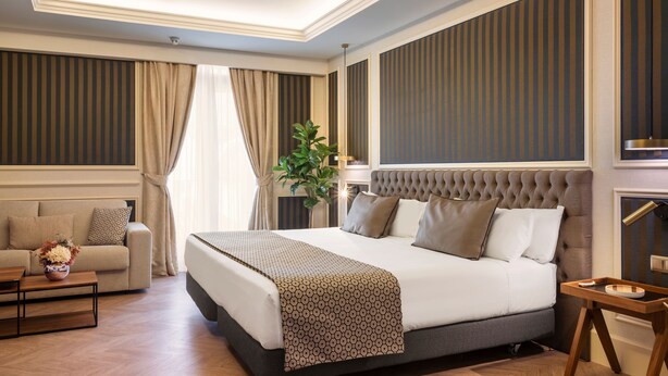Une chambre d’hôtel avec un grand lit, un canapé, une table basse en bois et une plante.