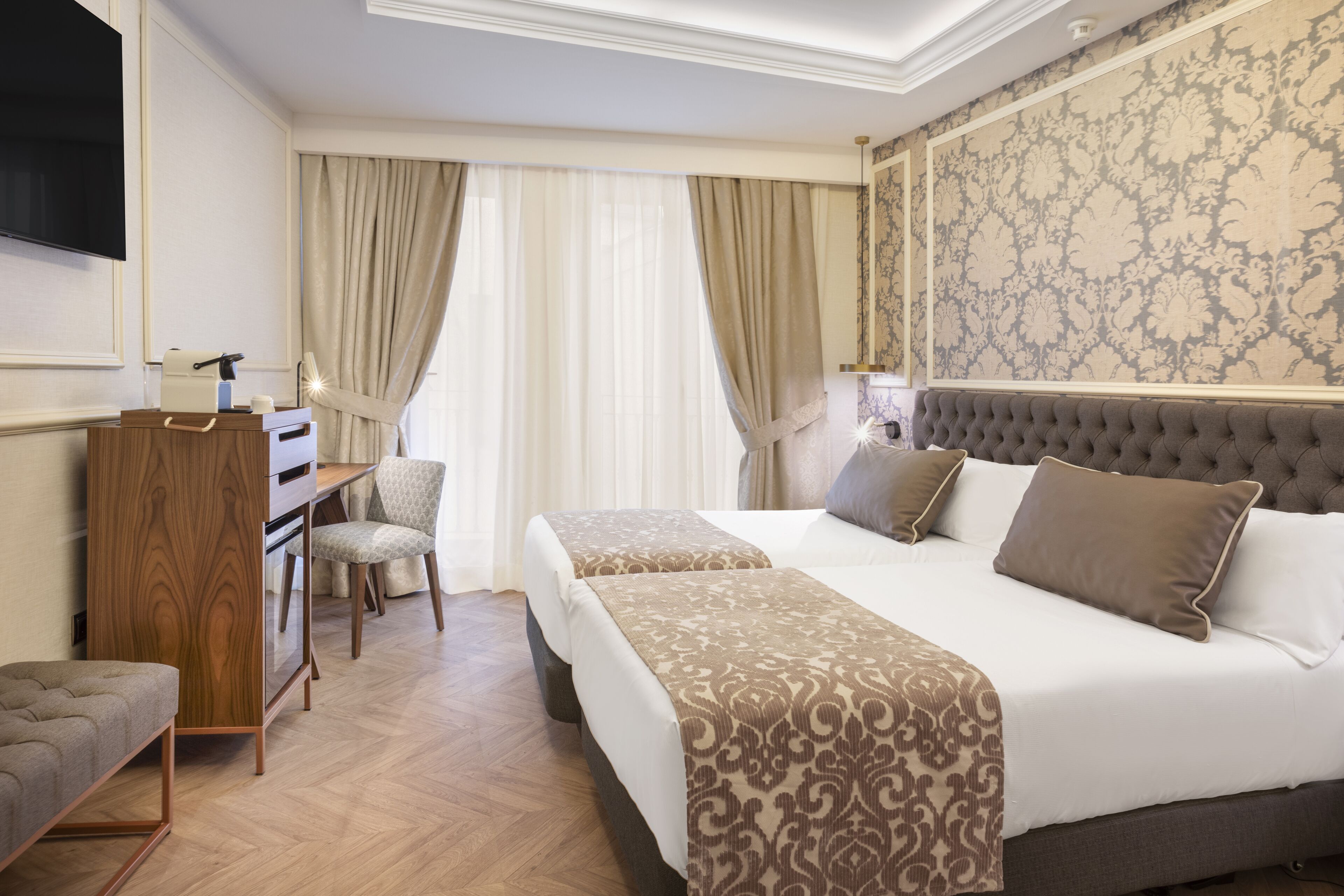 A hotel room with two beds, a desk, a chair, and a TV.