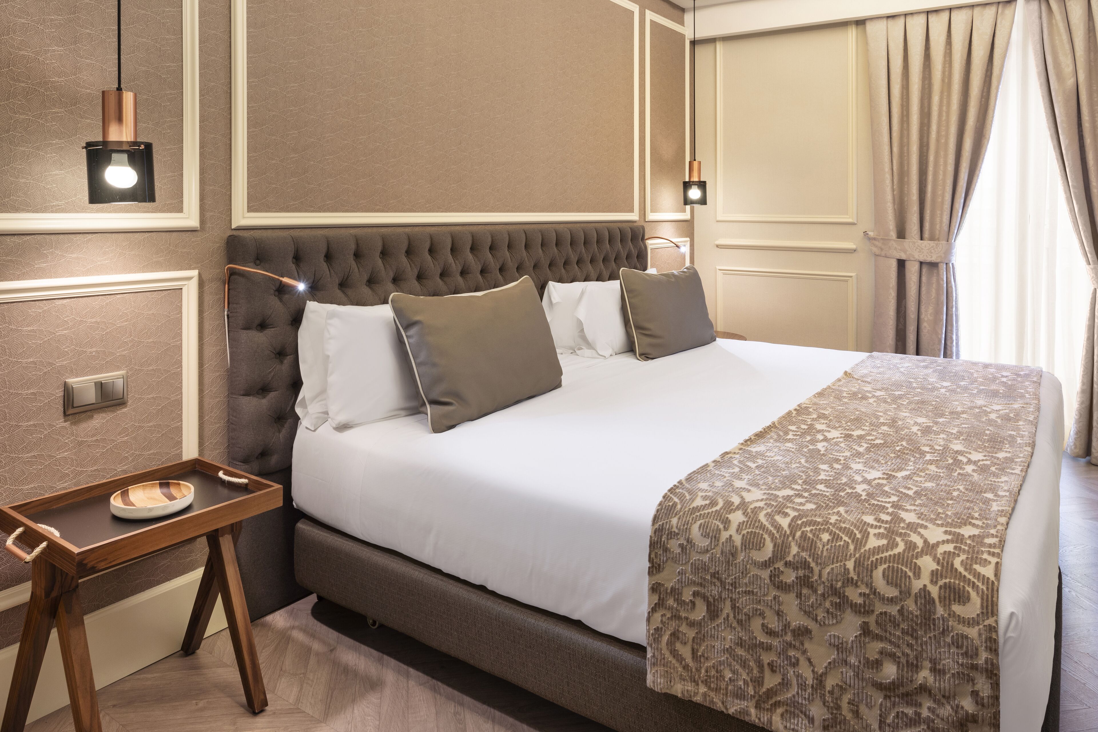 A neatly made bed with a patterned throw, a bedside table with a tray, and a modern pendant light.