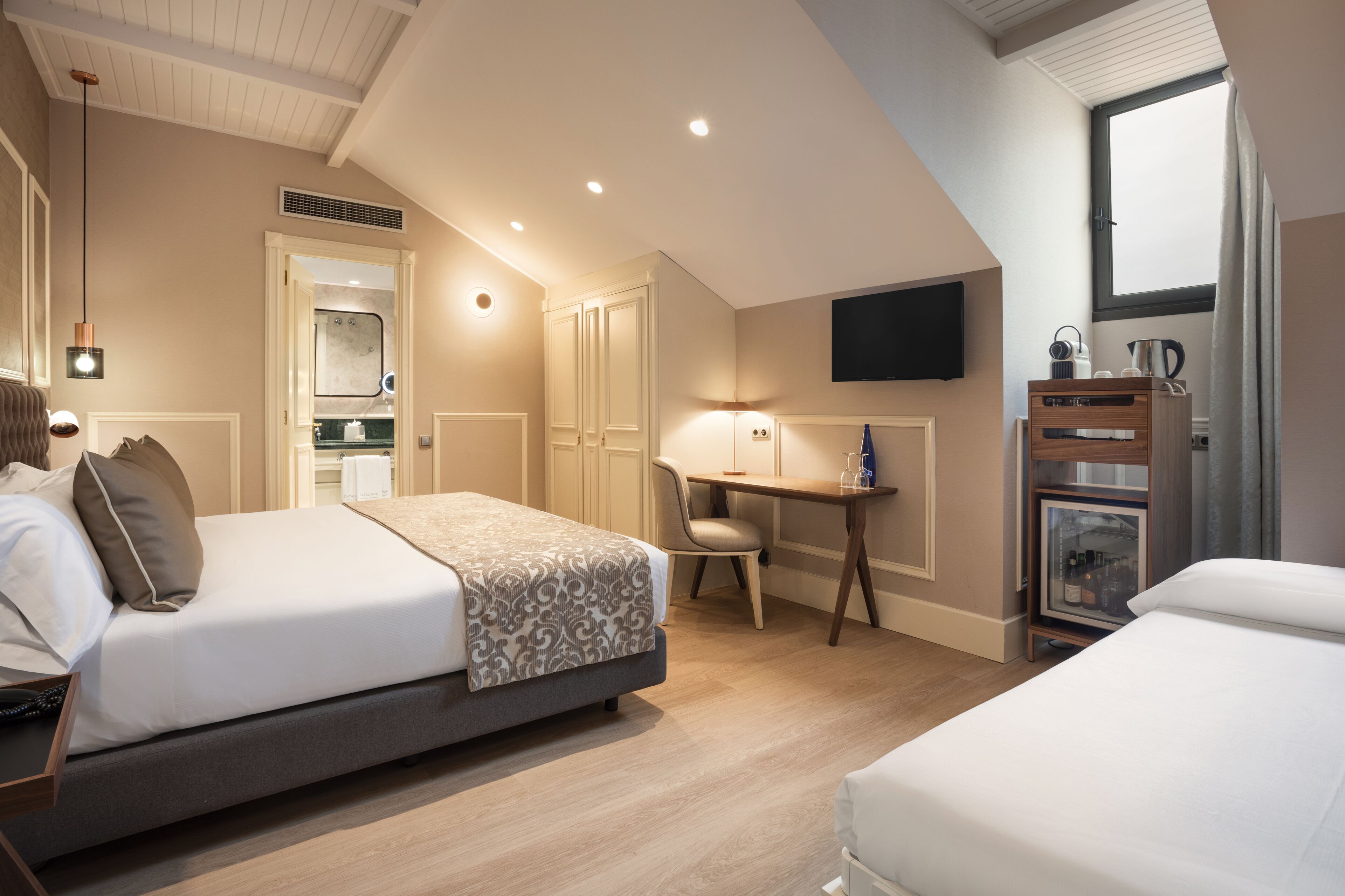 Une chambre d’hôtel équipée d’un lit, d’un bureau, d’une chaise et d’un téléviseur fixé au mur.