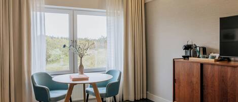 Une chambre d’hôtel comprenant un lit, une télévision, une armoire en bois, une table avec des chaises et une fenêtre avec des rideaux.