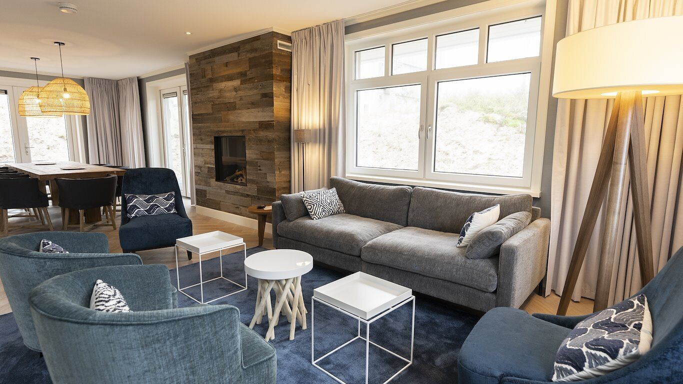 Una sala de estar moderna con un sofá gris, sillones azules y una pequeña mesa blanca.