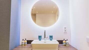 Ein Badezimmer mit einem rechteckigen Waschbecken, einem runden Spiegel und zwei blauen Tassen auf der Ablagefläche.