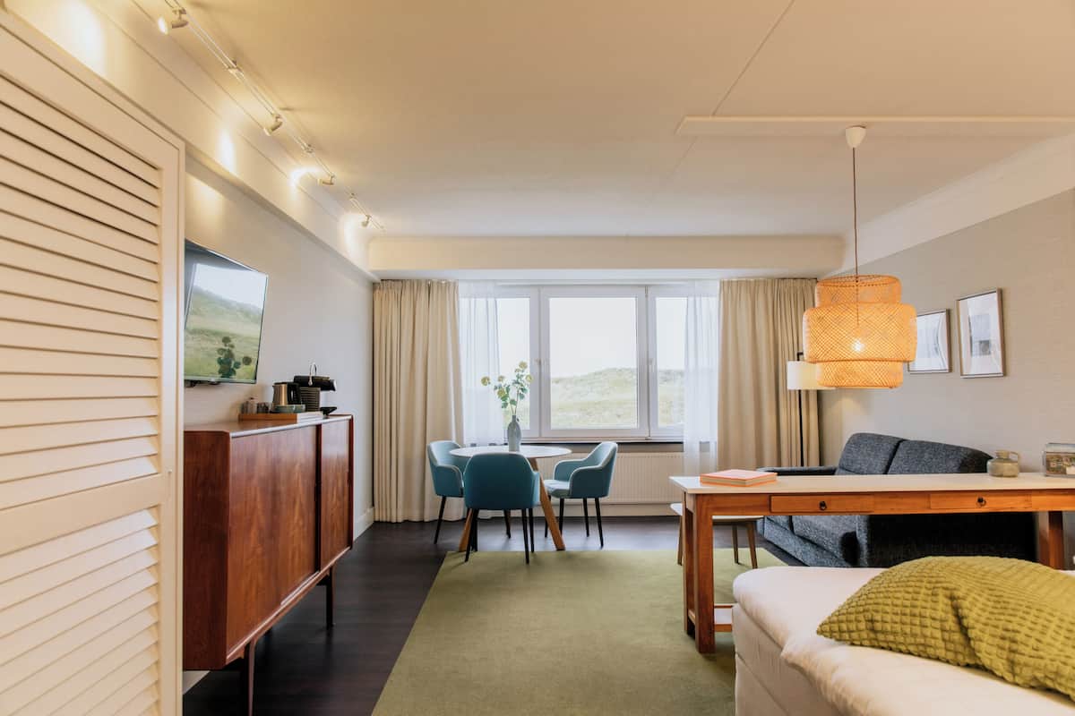 Een moderne hotelkamer met een zithoek, een bank en een groot raam met gordijnen.