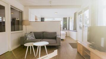 A modern living room with a grey sofa, two white side tables, a large flat-screen TV, and a wooden cabinet.