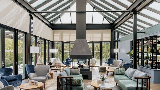 Un intérieur spacieux et bien éclairé, avec un plafond haut, de grandes fenêtres et différents types de sièges, notamment des canapés, des fauteuils et une cheminée.