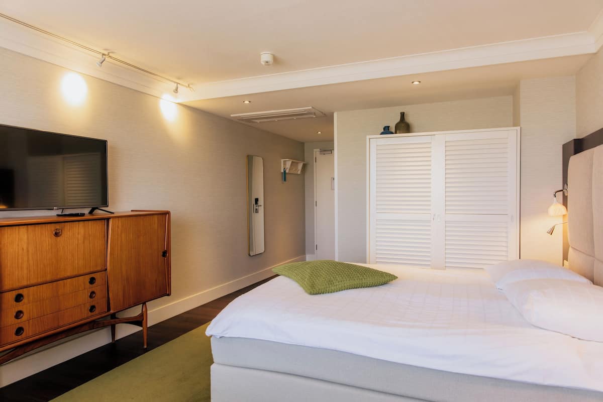 Een hotelkamer met een bed, een houten dressoir, een televisietoestel en een kast met witte luiken.