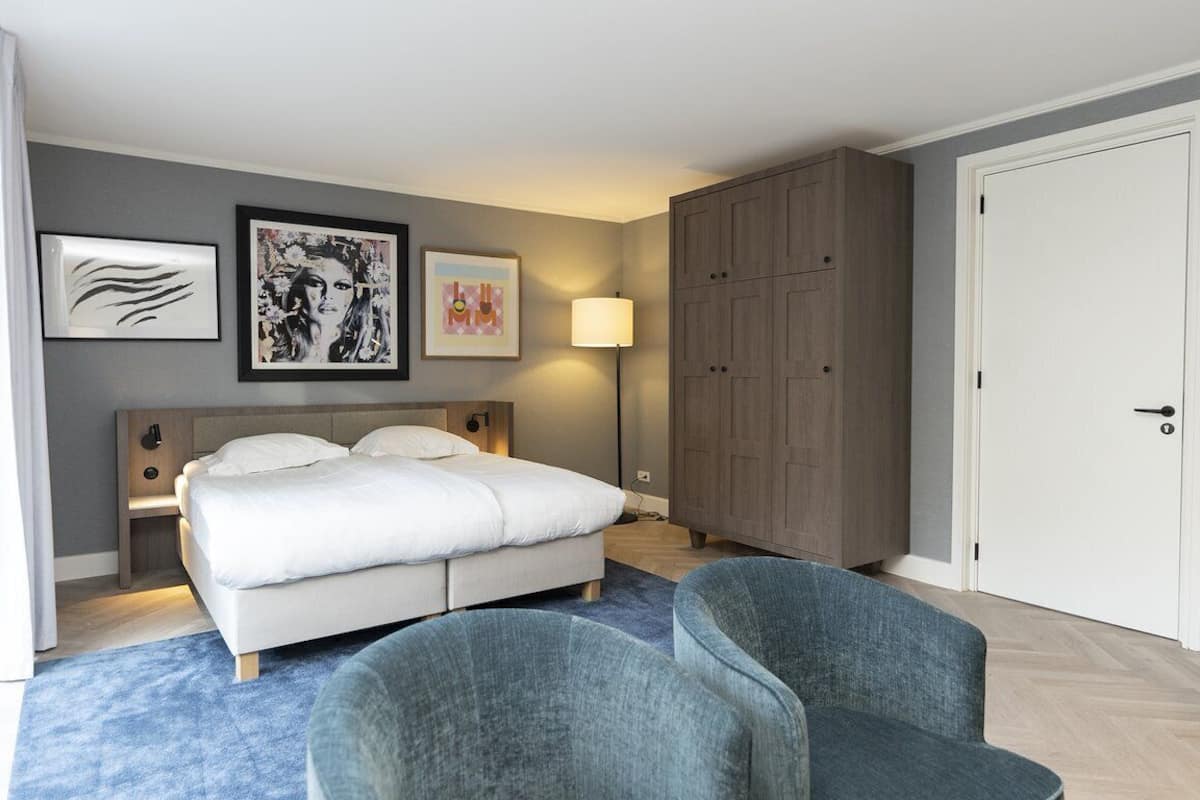 Een moderne slaapkamer met een bed, twee stoelen, een kledingkast en kunst aan de muur.