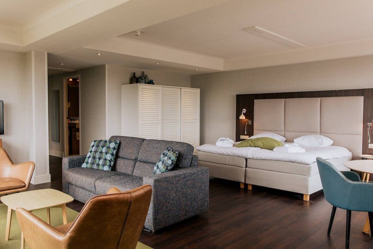 Een moderne hotelkamer met een bank, twee stoelen, een bed, een televisie en een kledingkast.