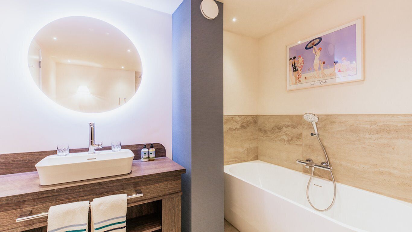 Ein modernes Badezimmer mit einem runden Spiegel, einem Waschbecken mit zwei Seifenspenden und einer Badewanne mit Duschkopf.