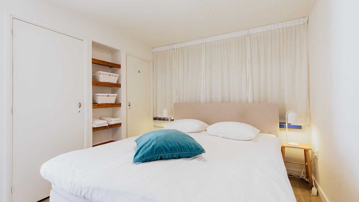 A hotel room with a bed, a nightstand, a lamp, a wardrobe, and a window with curtains.
