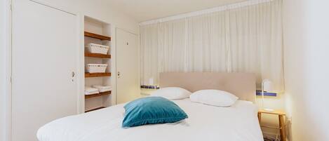 A hotel room with a bed, a nightstand, a lamp, a wardrobe, and a window with curtains.