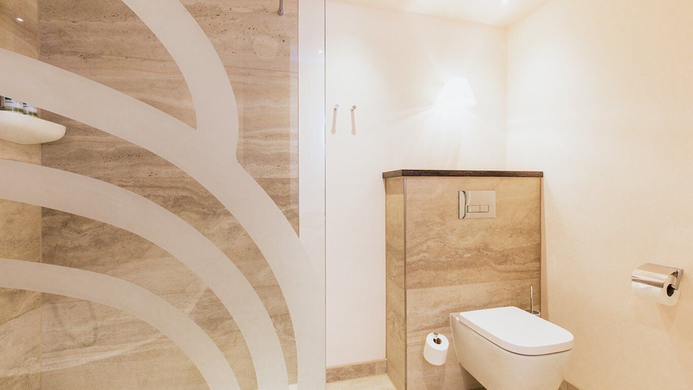 Een moderne badkamer met een marmeren wand, een toilet en een douche.
