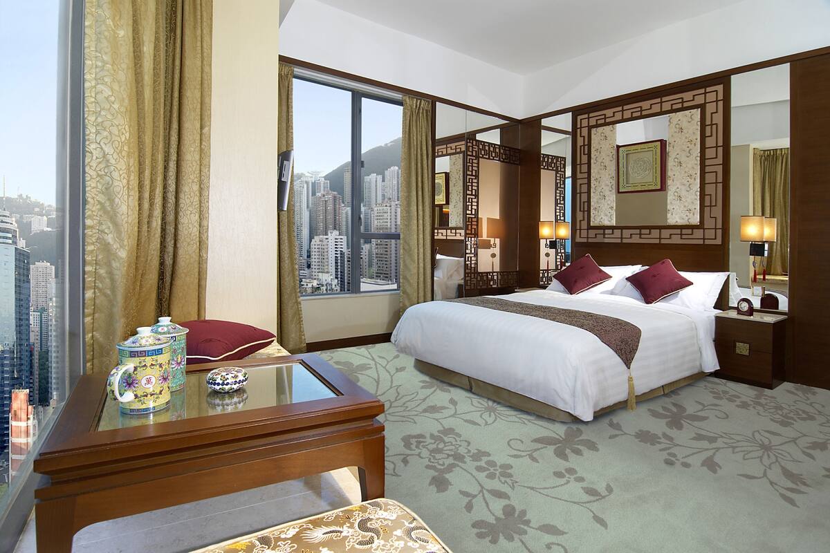 Ein Hotelzimmer mit einem großen Bett, einem Schreibtisch mit Teekanne und Blick auf die Stadt.