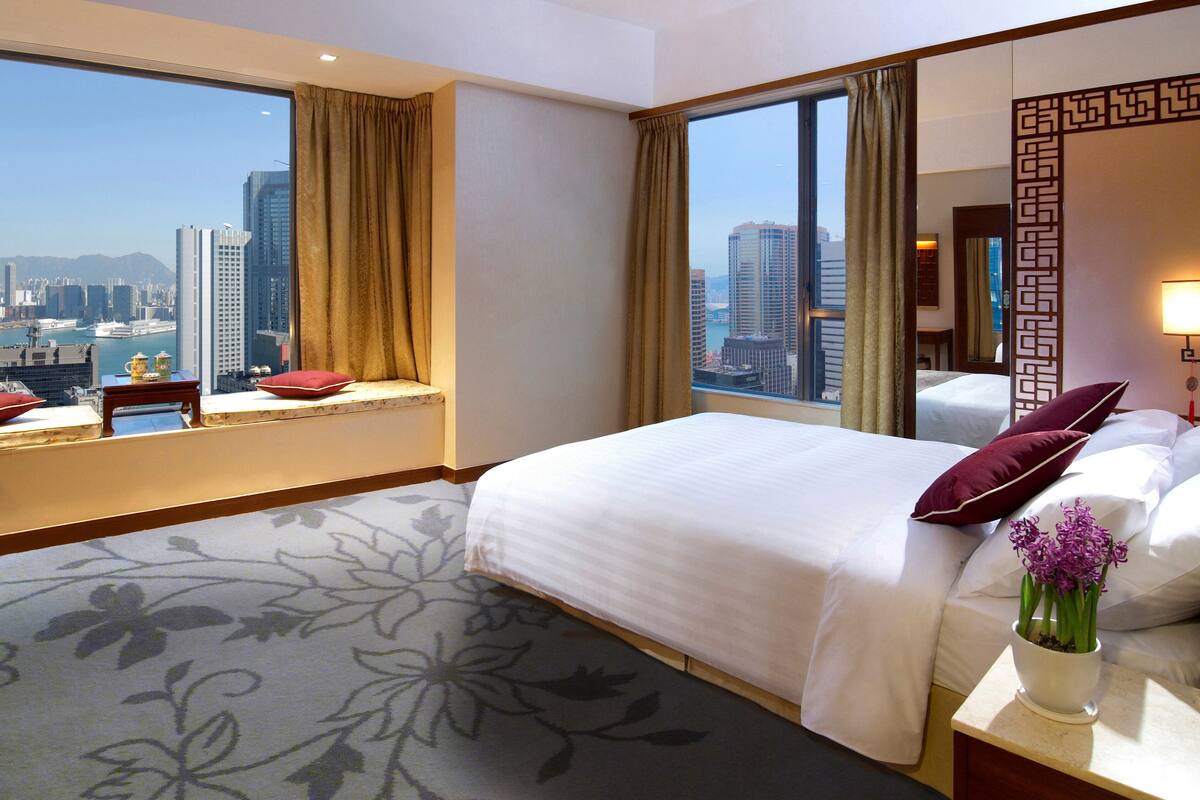 Ein Hotelzimmer mit einem großen Bett, einem Fenster mit Blick auf die Stadt und einem dekorativen Spiegel.