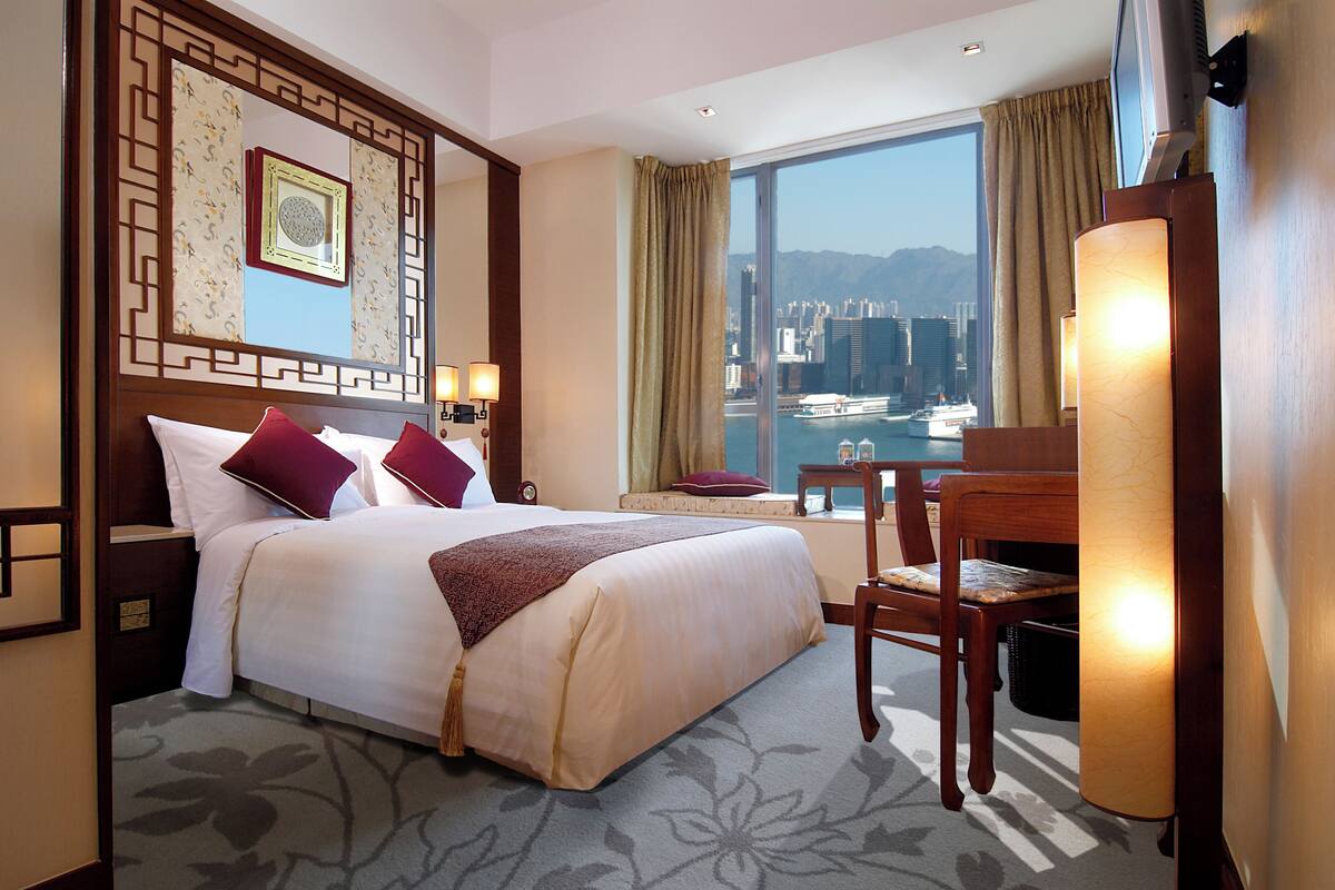Ein Hotelzimmer mit einem großen Bett, einem Schreibtisch und Blick auf eine Stadtansicht durch das Fenster.