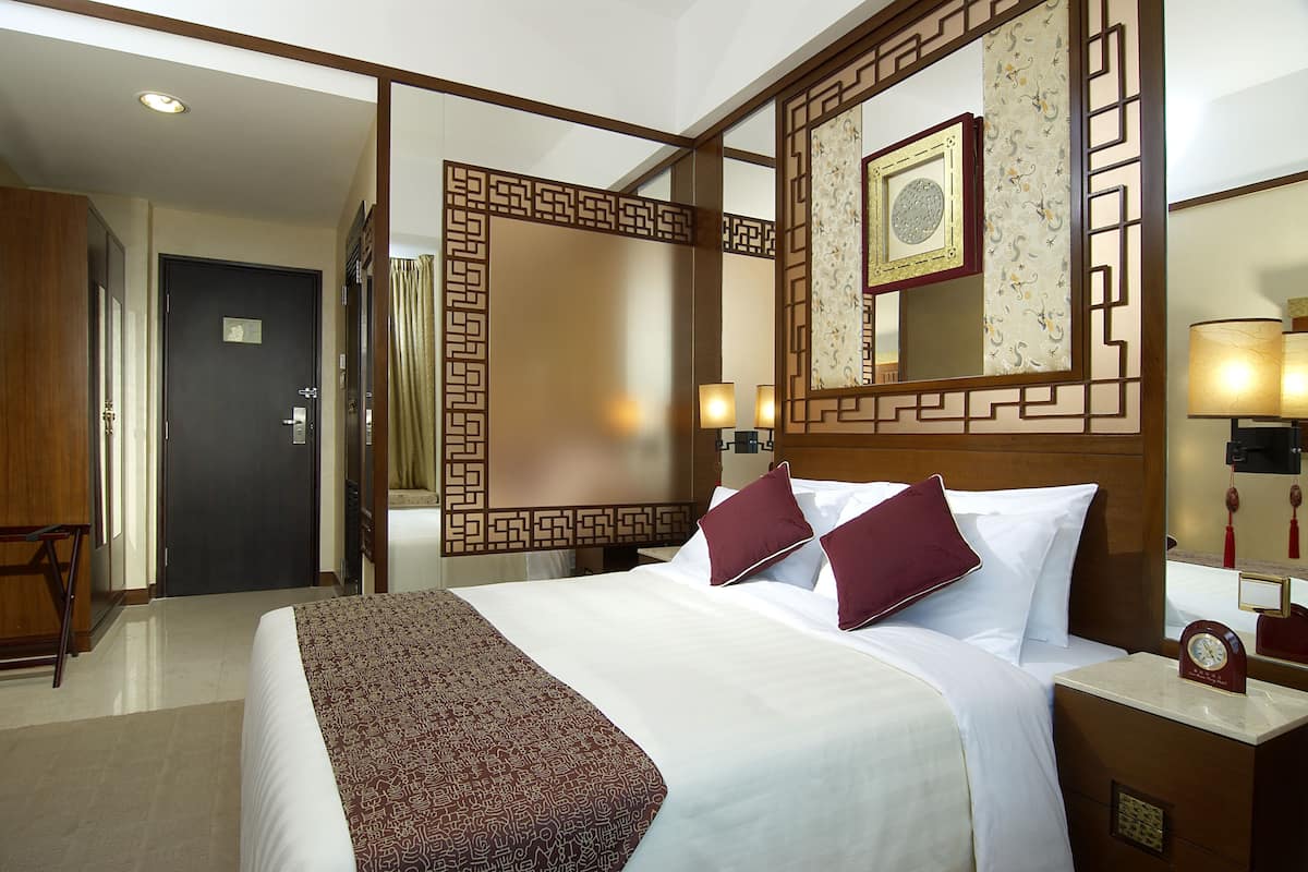 Ein Hotelzimmer mit einem großen Bett, zwei Nachttischlampen, einem hölzernen Kopfteil, einem Spiegel und einer Uhr auf dem Nachttisch.