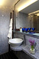 A bathroom with a white sink, a glass shelf with blue bowls, a towel rack, and a mirror.