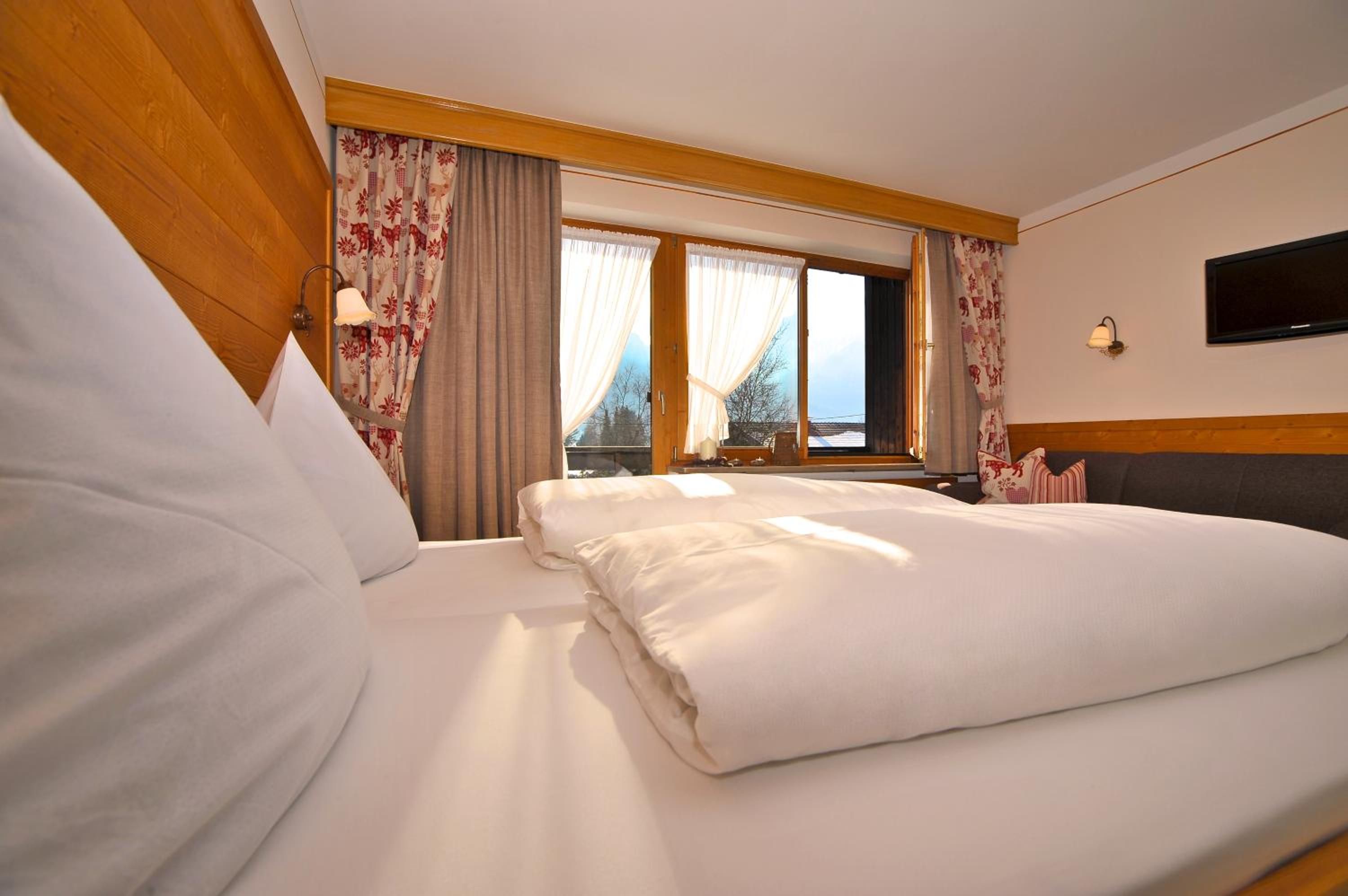 Ein Hotelzimmer mit einem großen Bett, einem an der Wand montierten Fernseher und einem Fenster mit Vorhängen.