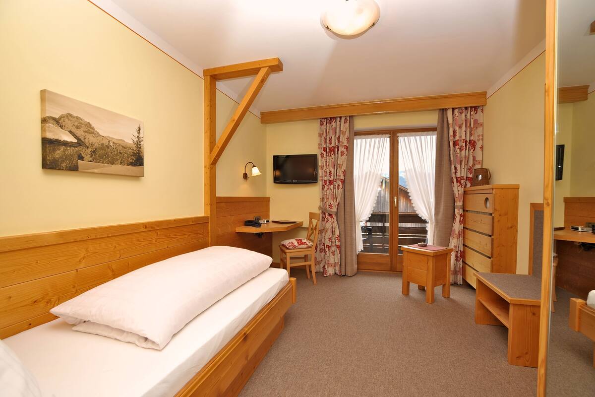 Ein Schlafzimmer mit Bett, Schreibtisch, Stuhl, Fernseher und einem Bild an der Wand.
