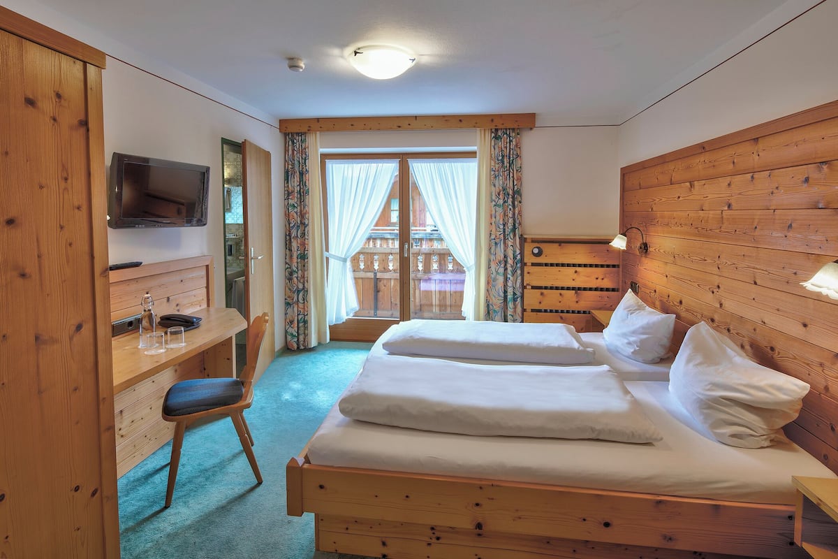 Ein Zimmer mit Holzboden, einem Bett, einem Schreibtisch, einem Fernseher und einem Fenster mit Vorhängen.