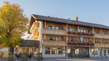 Un hôtel à plusieurs étages, doté d’une façade traditionnelle en bois, de balcons ornés de jardinières et d’une entrée au niveau du sol.