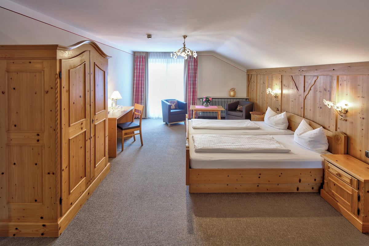 Ein Schlafzimmer mit einem großen Bett, einem Holzschrank, einem Schreibtisch, einem Stuhl und einem kleinen Tisch mit Lampe.