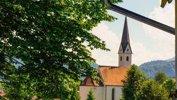 En kirke med et spidsfindigt spir og et klokketårn, omgivet af træer og et bjerg i baggrunden.