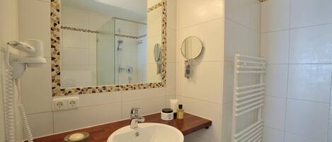 Un baño con lavamanos blanco, espejo, secador de pelo y toallero.