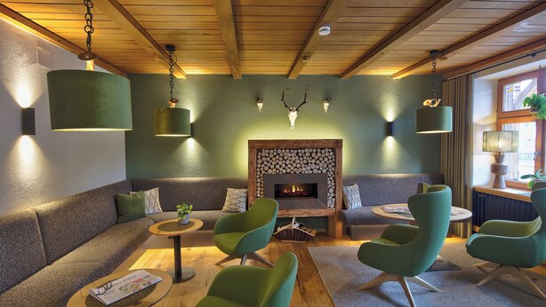 Uma área de estar acolhedora com poltronas estofadas em verde, teto de madeira e lareira com um painel decorativo ao fundo.