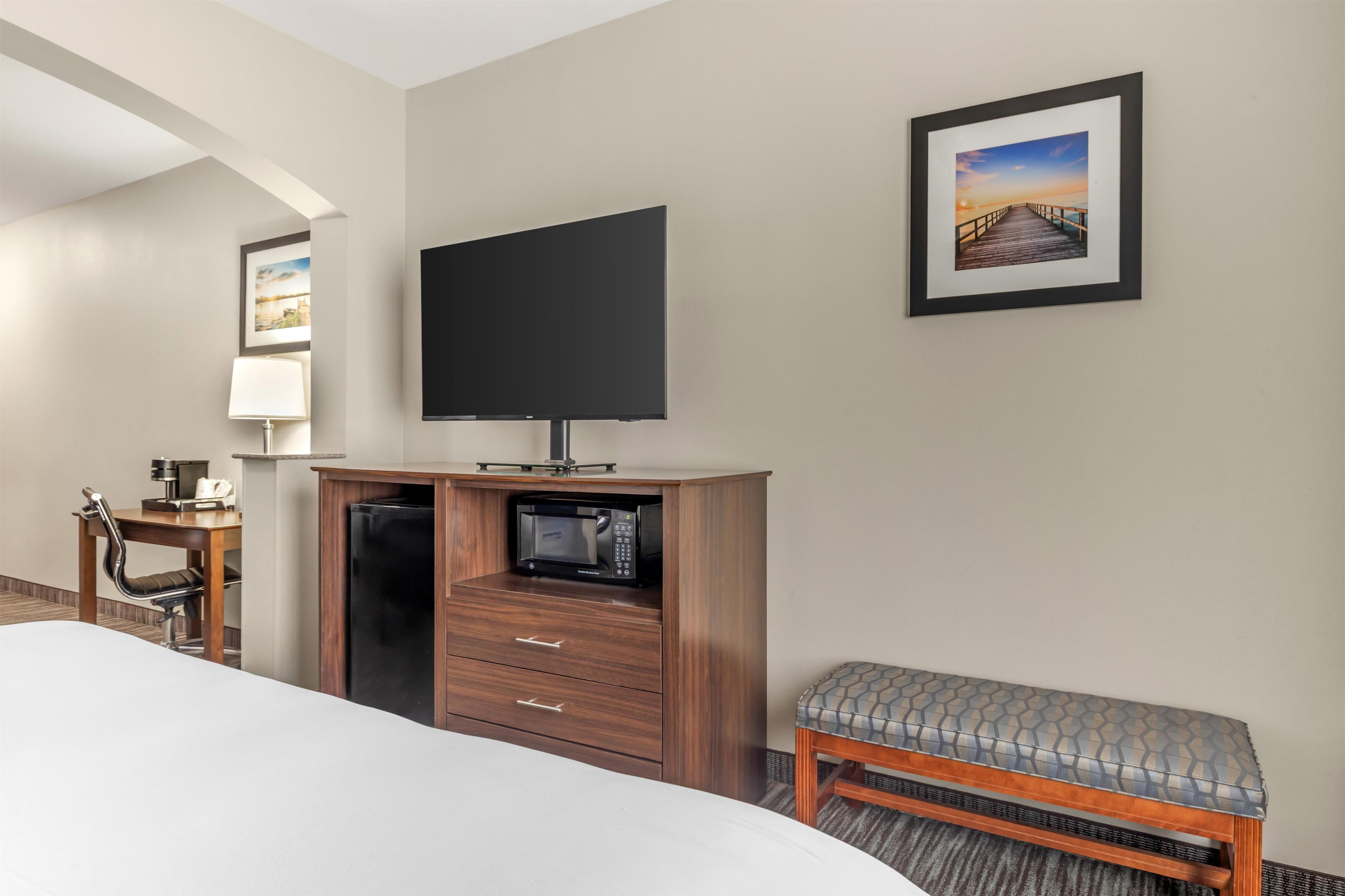 Habitación de hotel con una cama, un televisor de pantalla plana montado en un mueble de madera, un escritorio con una lámpara, una silla y un banco.