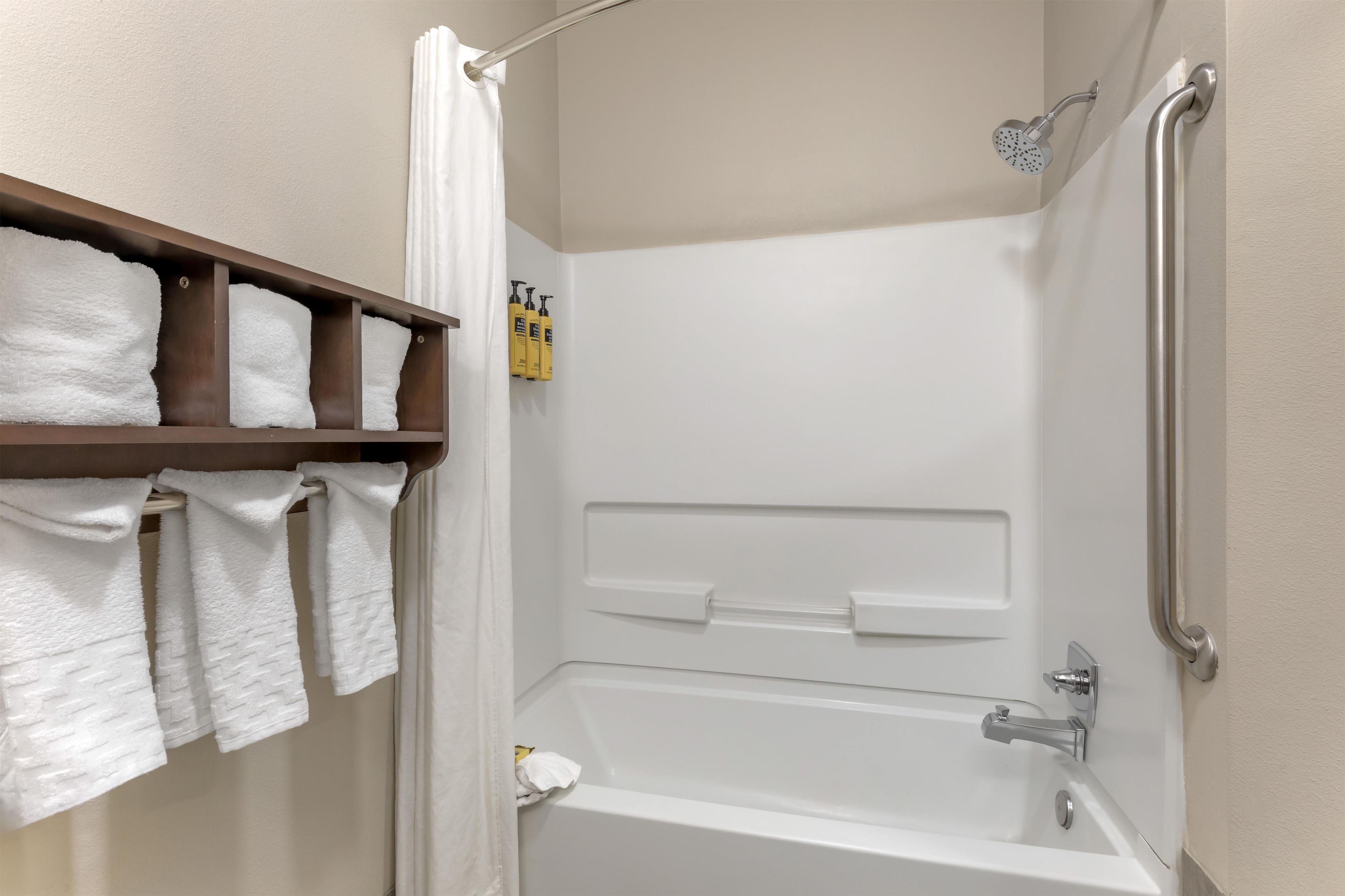 A bathroom with a bathtub, a shower, a handrail, and a shelf with towels.