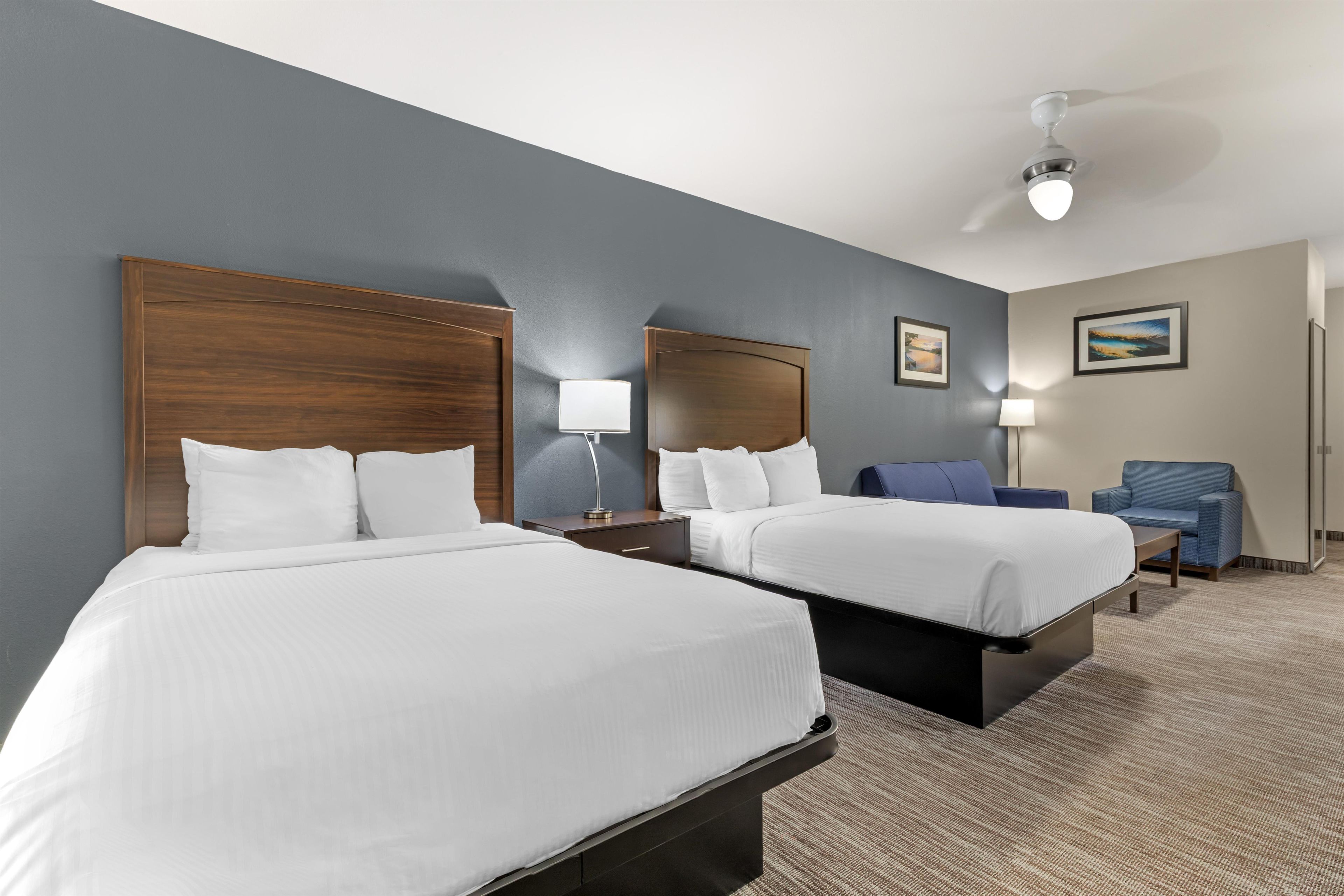 Habitación de hotel con dos camas, un escritorio, una silla, una lámpara y un ventilador de techo.