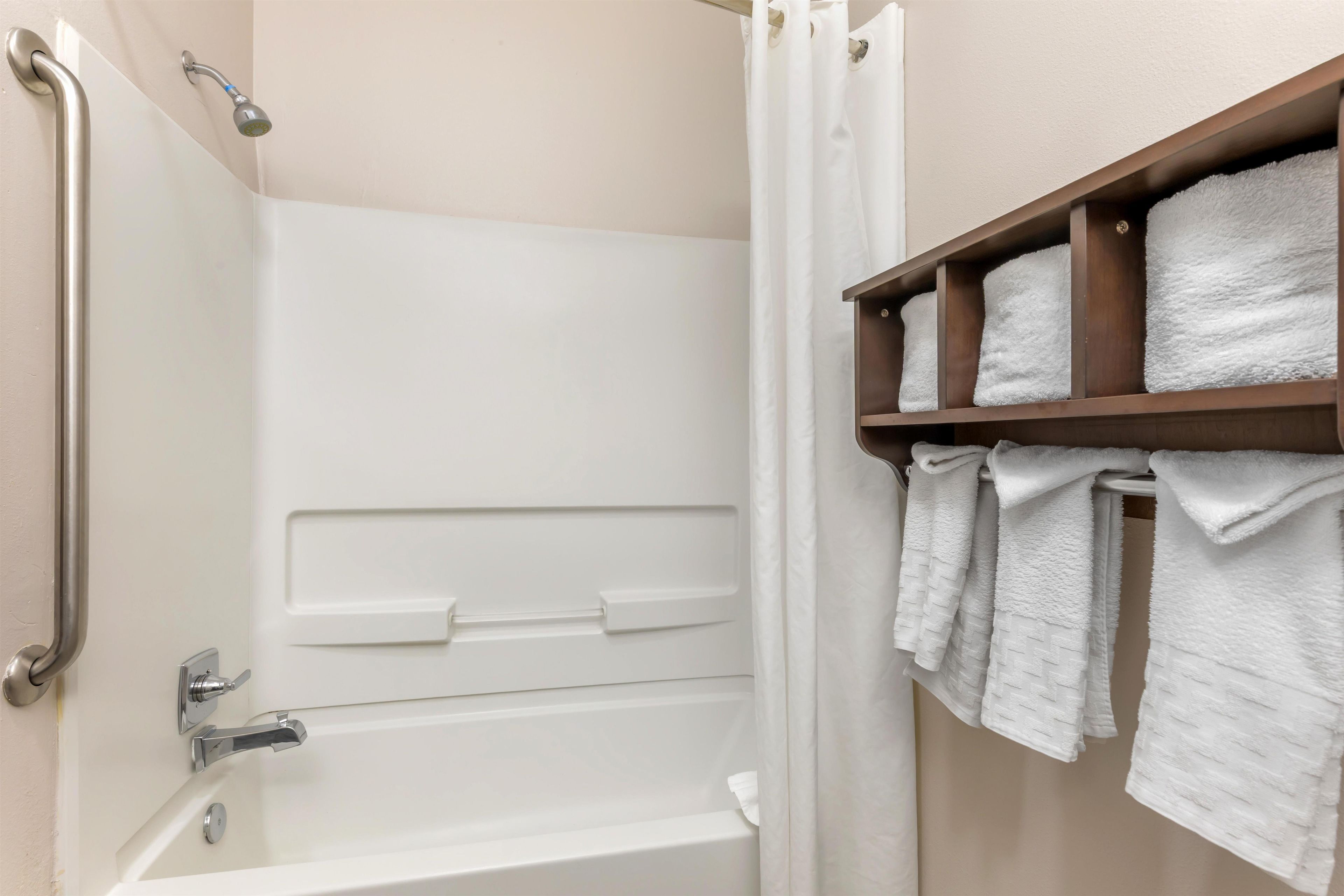 A bathroom with a white bathtub, a shower, and a towel rack with neatly folded towels.