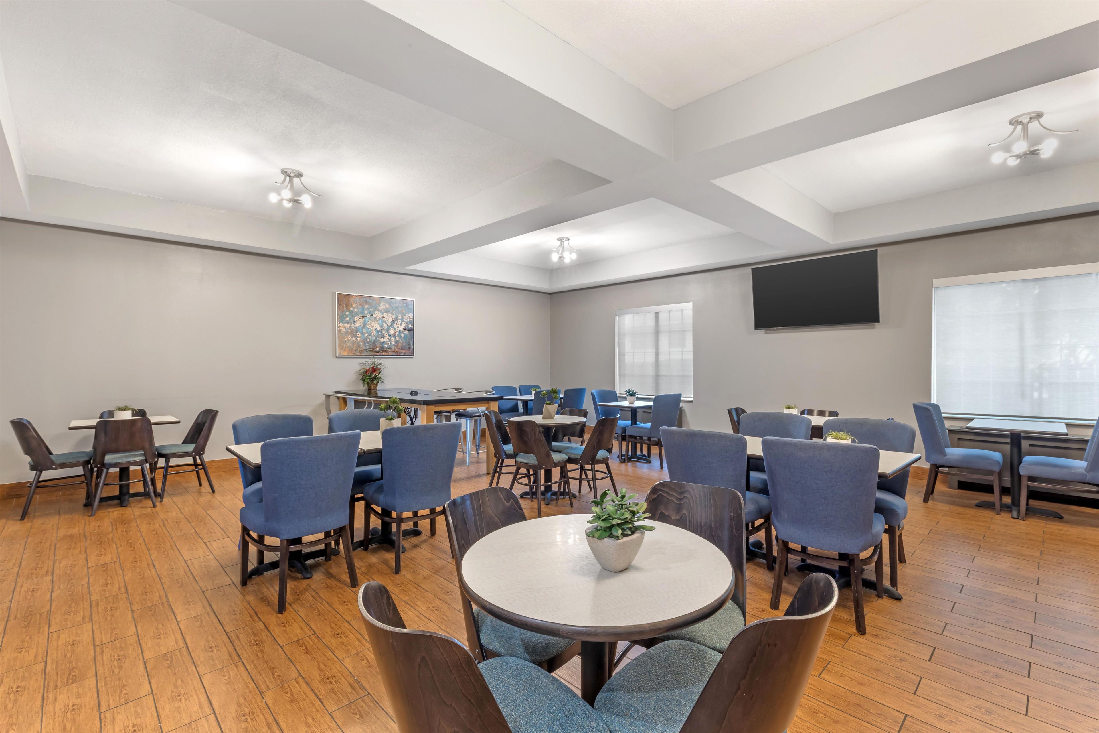 A conference room with round tables and chairs, a large screen, and a painting on the wall.