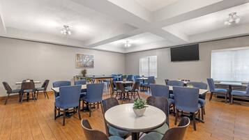 A conference room with round tables and chairs, a large screen, and a painting on the wall.