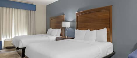 Habitación de hotel con dos camas, una mesita de noche, una lámpara y un ventanal con cortinas.