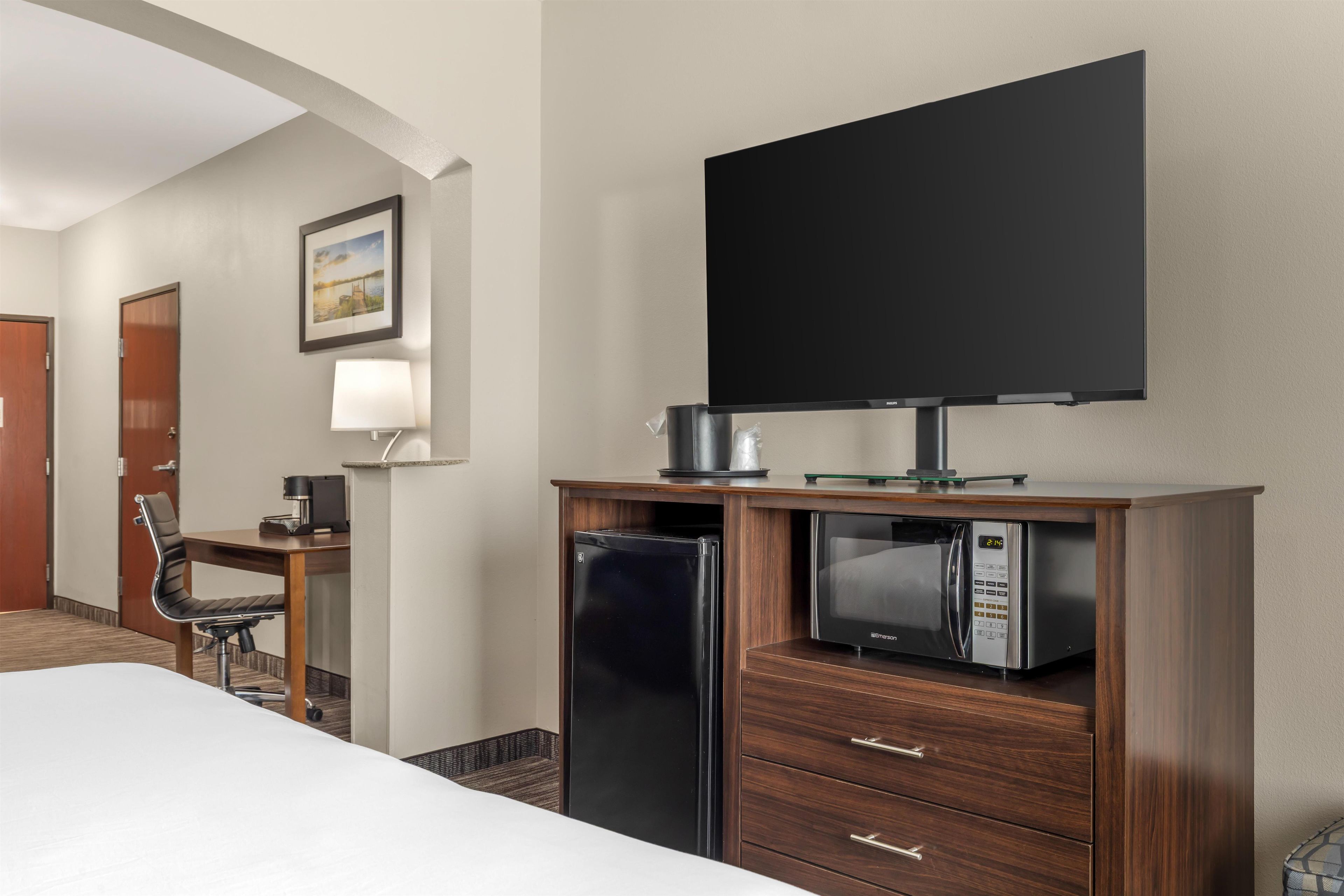 A hotel room with a bed, a desk with a coffee maker, a microwave, and a television on a stand.