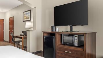 A hotel room with a bed, a desk with a coffee maker, a microwave, and a television on a stand.