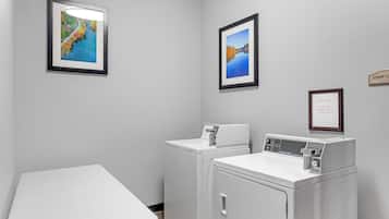 A laundry room with two washing machines, a drying machine, and two framed pictures on the wall.