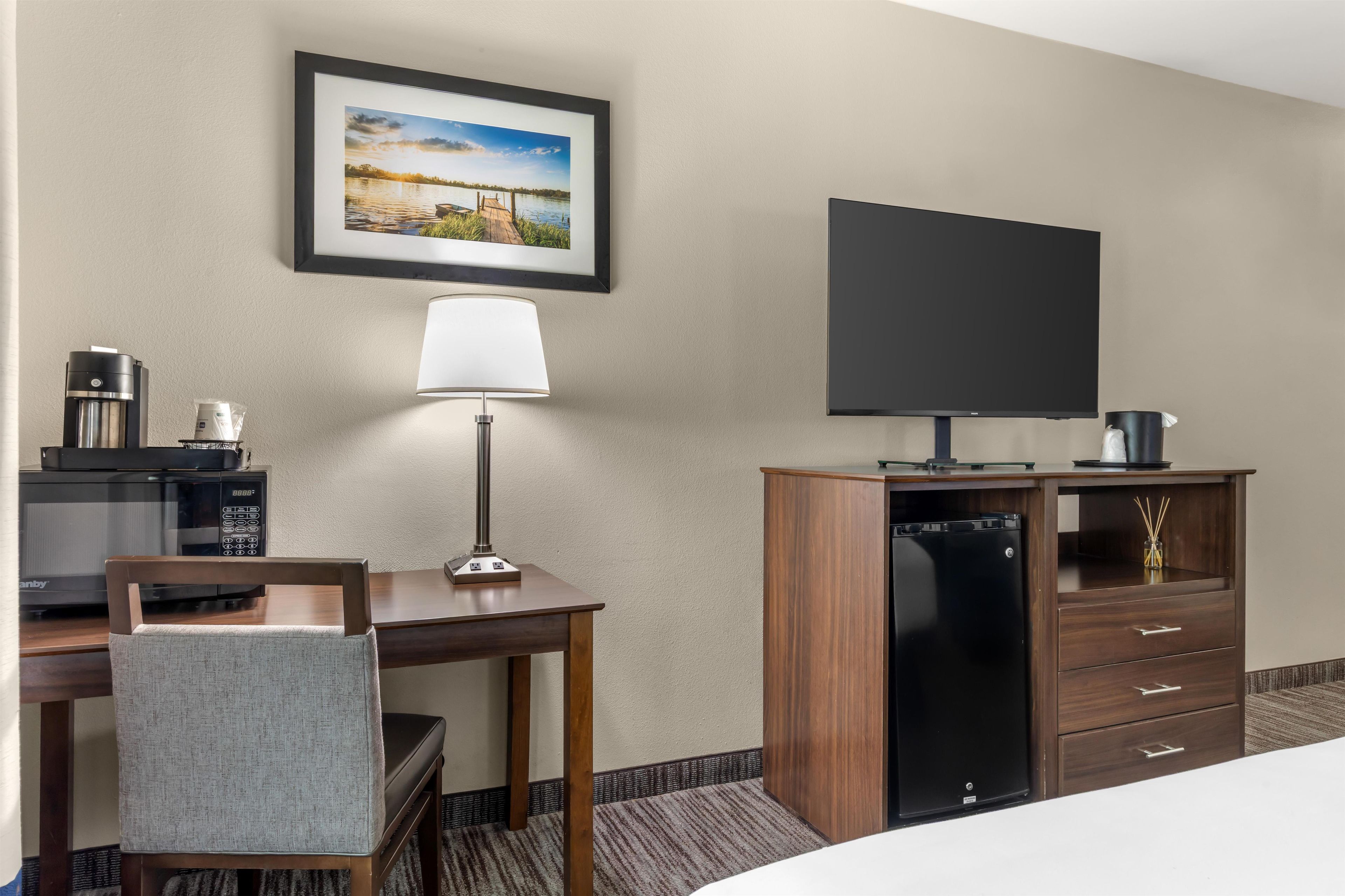 Habitación de hotel con cama, escritorio con lámpara, televisor, cafetera y minibar.