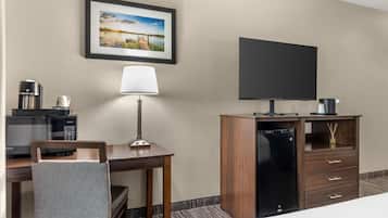 Habitación de hotel con cama, escritorio con lámpara, televisor, cafetera y minibar.
