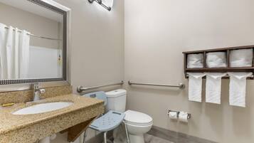 A bathroom with a granite countertop sink, a mirror with a decorative frame, a toilet, a grab bar, and a shelf with towels.
