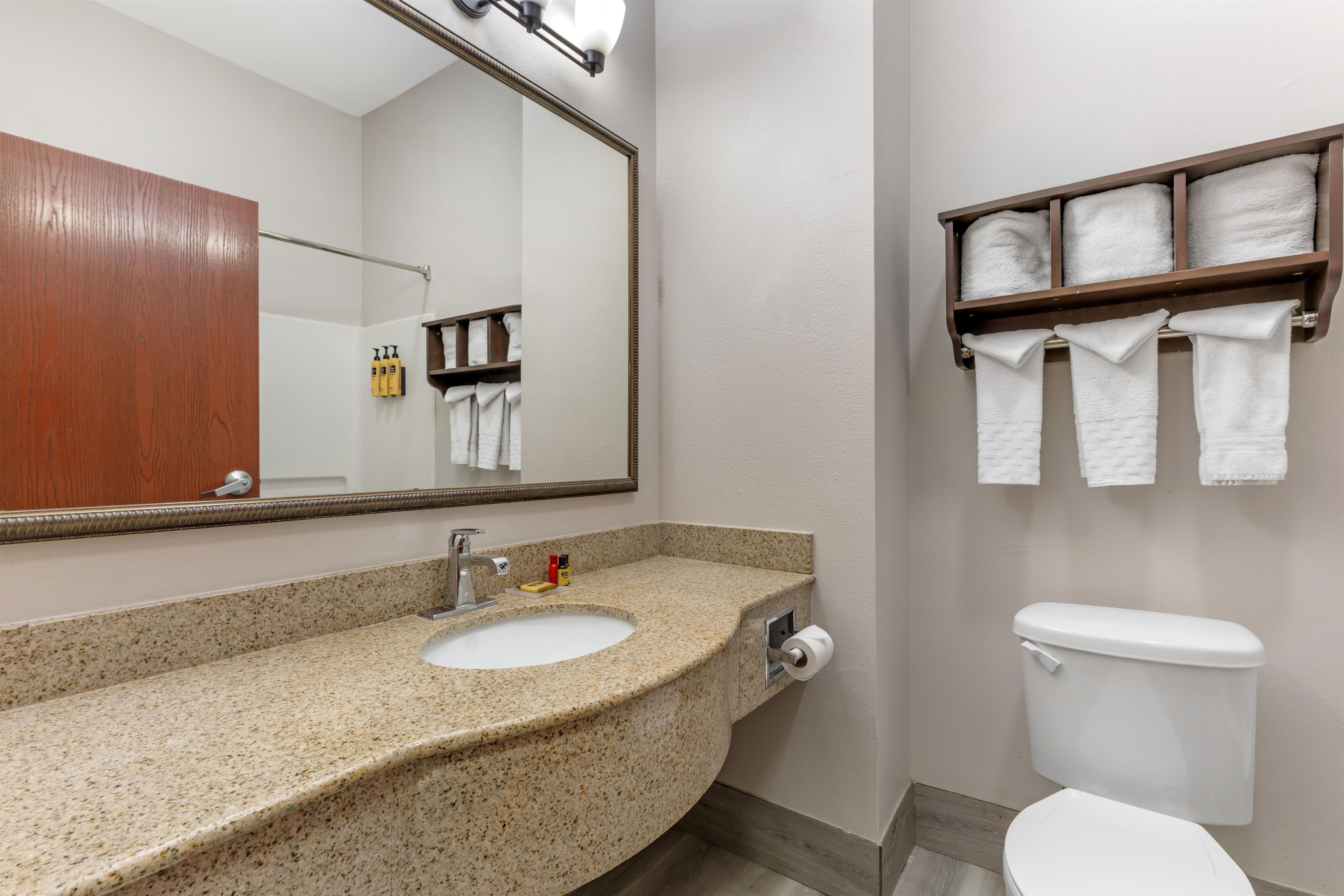 A bathroom with a granite countertop sink, a mirror, a toilet, and a towel rack with towels.