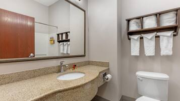 A bathroom with a granite countertop sink, a mirror, a toilet, and a towel rack with towels.
