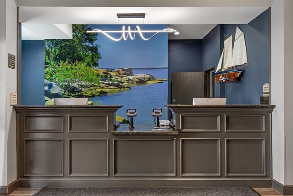 A reception area with a large scenic mural, a wooden desk, a small sailboat model, and a 'Manager on Duty' sign.